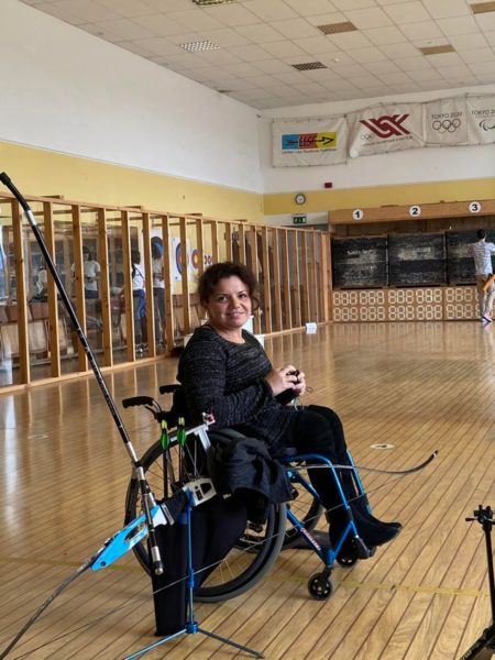  Iryna Zubova with her wheelchair at the indoor shooting club posing with her bow and arrows.