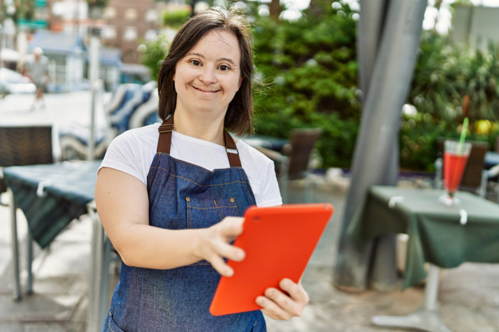 Young down syndrome womanusing touchpad and working coffee shop terrace