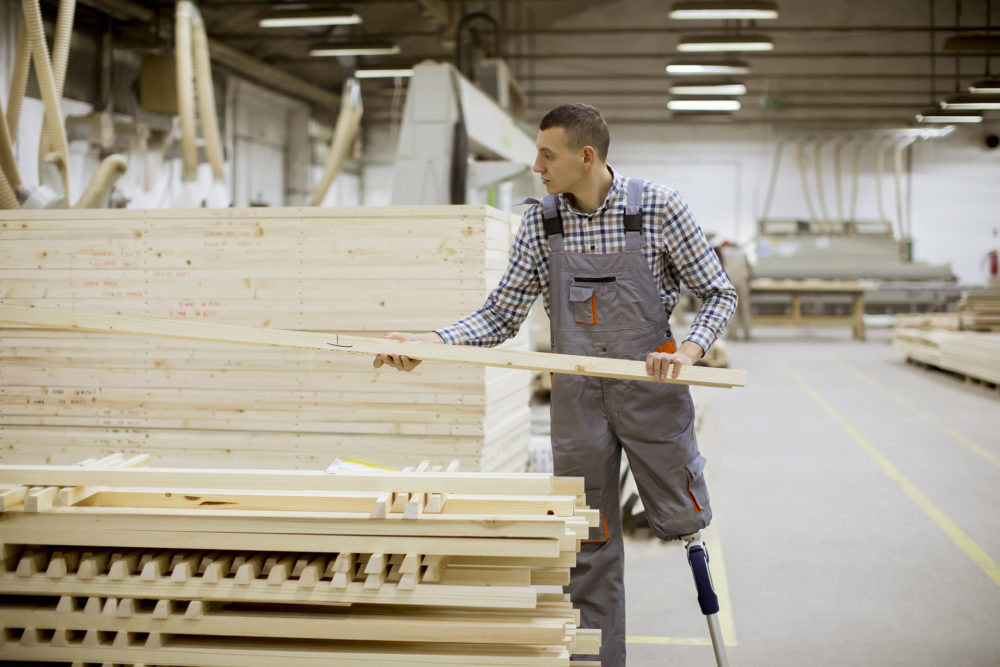 young man with an artificial leg is arranging wooden palletsat the furniture factory