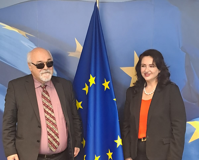 EDF President Yannis Vardakastanis stands next to Commissioner Dalli with a EU flag in the background.