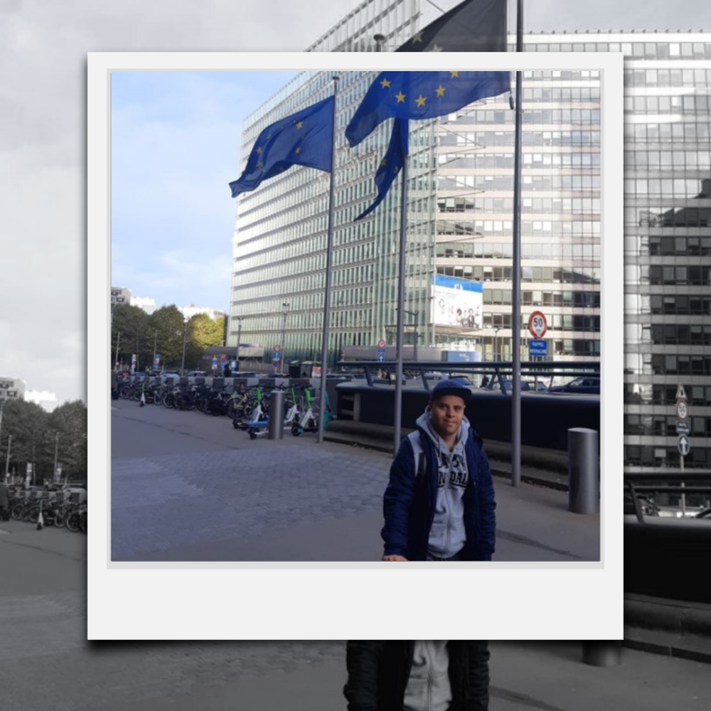 Dávid Aranyos in Brussels in front of 2 EU flags.