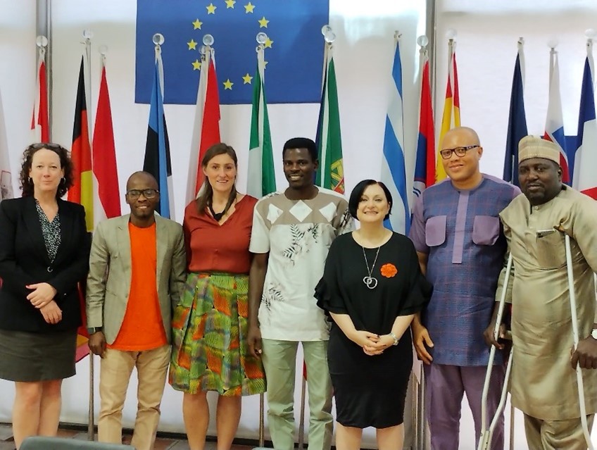 Group picture: Phillipa and the EU Delegation in Abuja staff pose in front of national flags and an EU flag