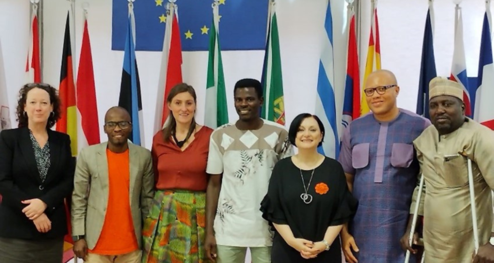 Group picture: Phillipa and the EU Delegation in Abuja staff pose in front of national flags and an EU flag