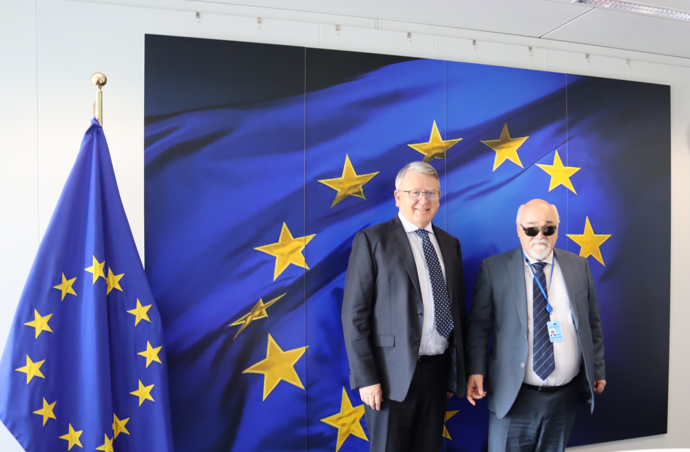 EDF President Yannis Vardakastanis posing next to Nicolas Schmit with a EU flag in the background