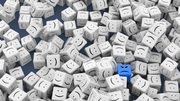 A blue angry smiley face in the middle of a group of white happy cubes