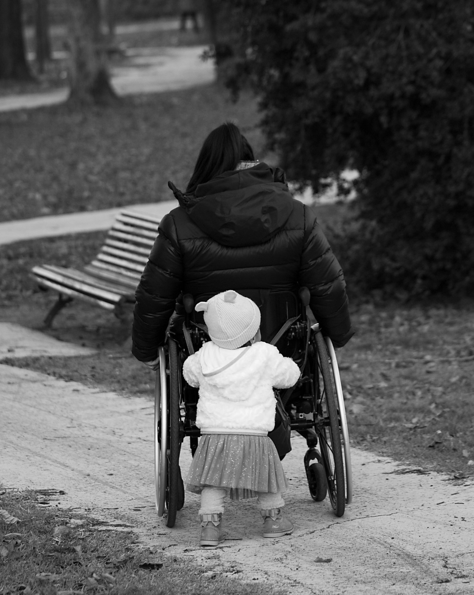 Black and white photo of a mother and daughter. The daughter tenderly pushes her mother's wheelchair.