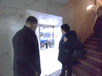 A group of people standing at the entrance of an elevator, and a man in a wheelchair inside the elevator.