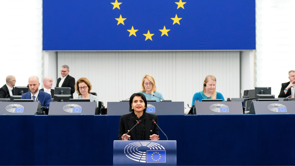 MEP Abir Al-Sahlani wears a black dress while speaking from the podium. She faces the camera, and behind her, there is a raised platform with the Parliament's Vice-Presidents.