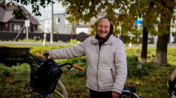 A older women smiles while holding a bicycle
