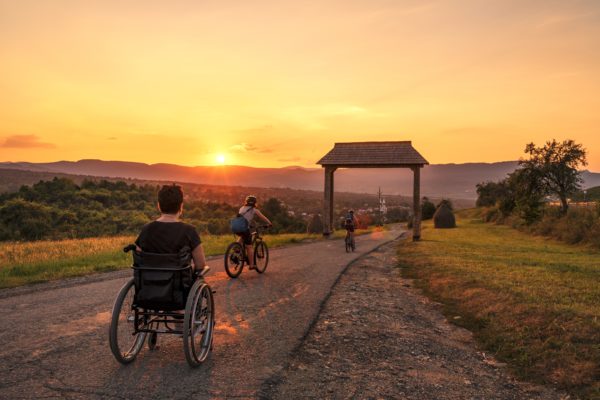 Persons in wheelchairs going on a road towards the sunset