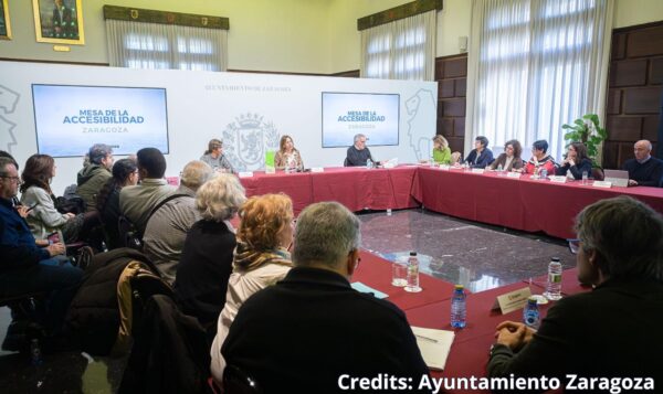 A group of representatives accross a table with screens saying "Accessibility Board" in Spanish